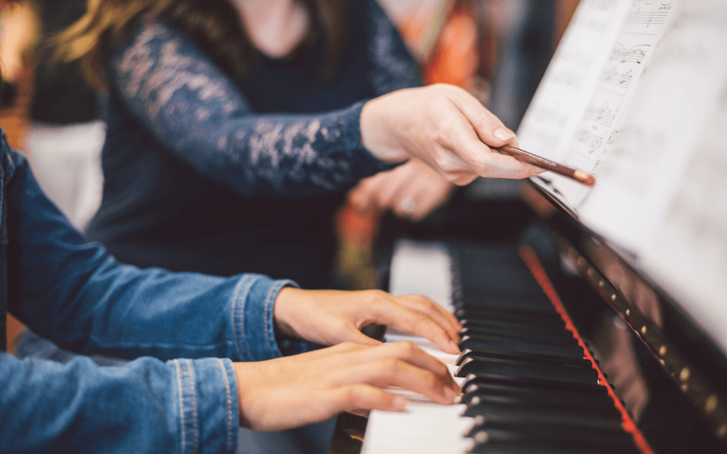 A closeup of an adult teaching a child the piano, only their hands and arms are visible.