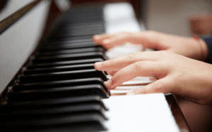 A closeup of black and white piano keys being played by a child, only their hands are visible.